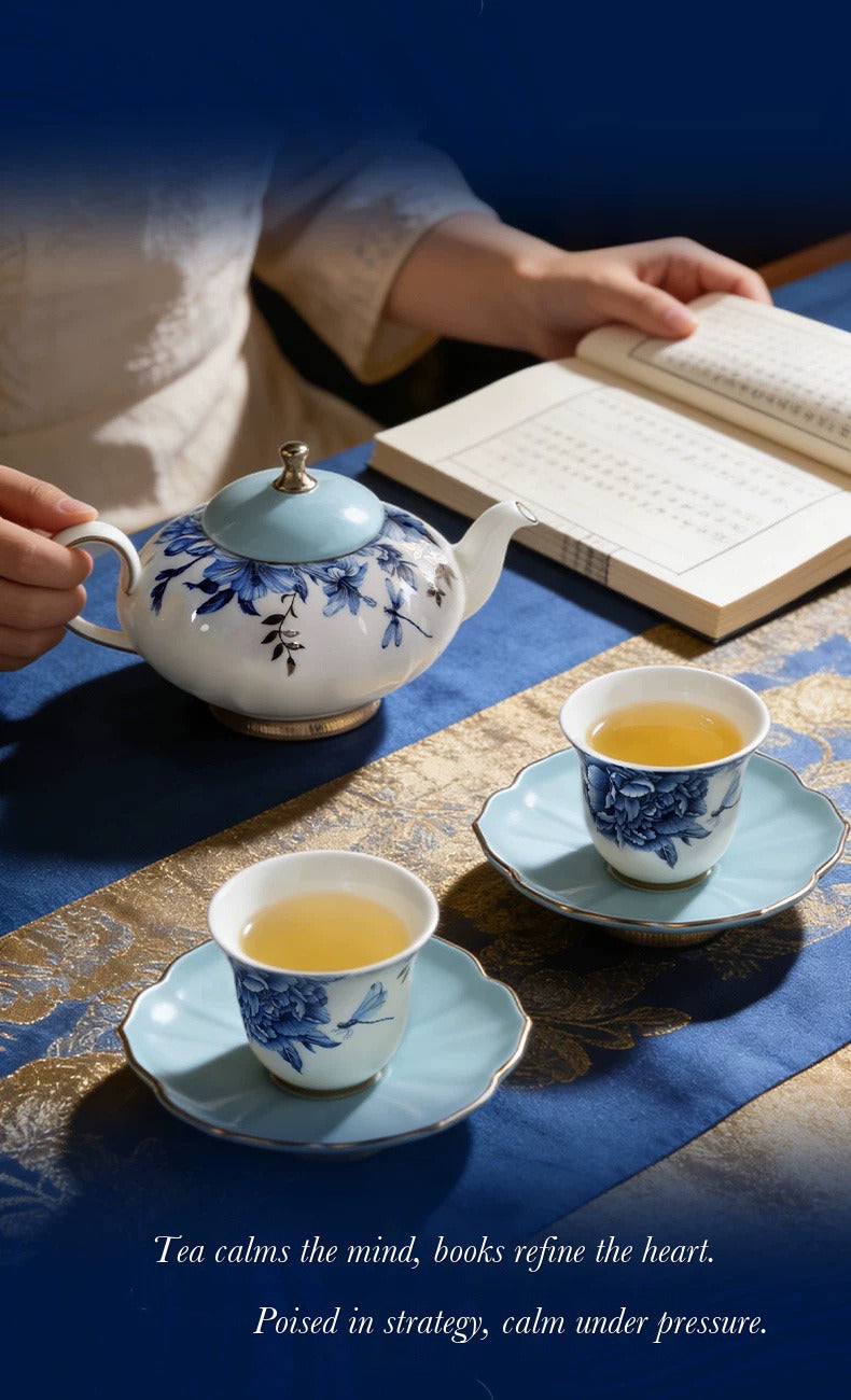 Pouring tea from a blue-and-white porcelain teapot beside an open book and two teacups